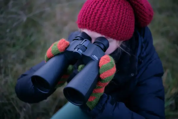 Dziewczyna w czerwonej czapce i rękawiczkach obserwuje niebo przez lornetkę Pentax. Idealna lornetka do obserwacji nieba.